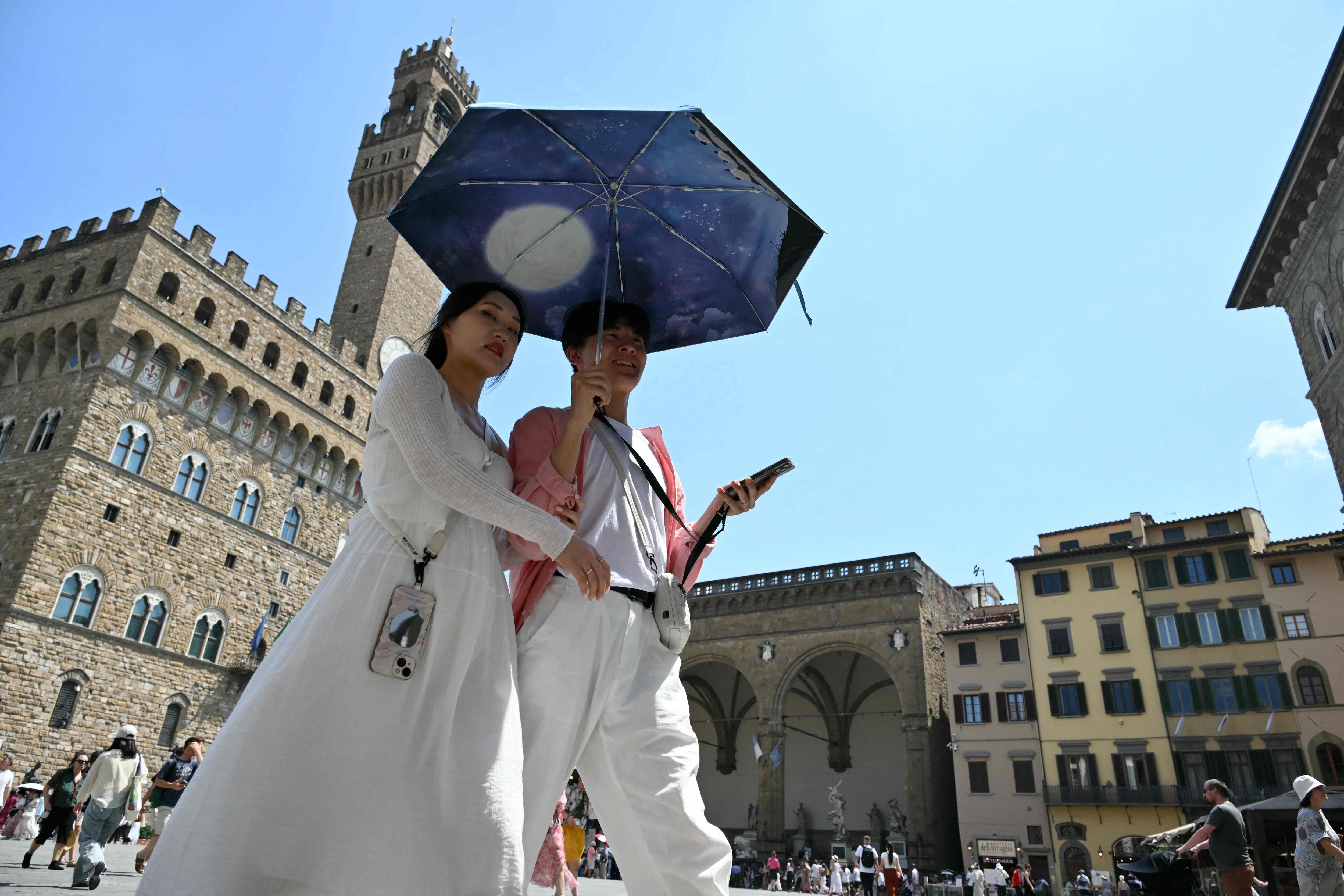 Un couple se protège du soleil sous un parasol en traversant la Piazza della Signoria à Florence, lors d'une vague de chaleur le 24 juin 2026.
