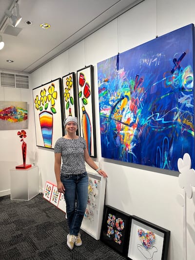 La artista Mélanie Simard posa con varios de sus cuadros que estarán disponibles durante la Noche de las Galerías. El lienzo de la derecha (azul) se titula “Siempre hay esperanza” y el de la izquierda (dorado) se titula “Nuestras preciosas luchas”.