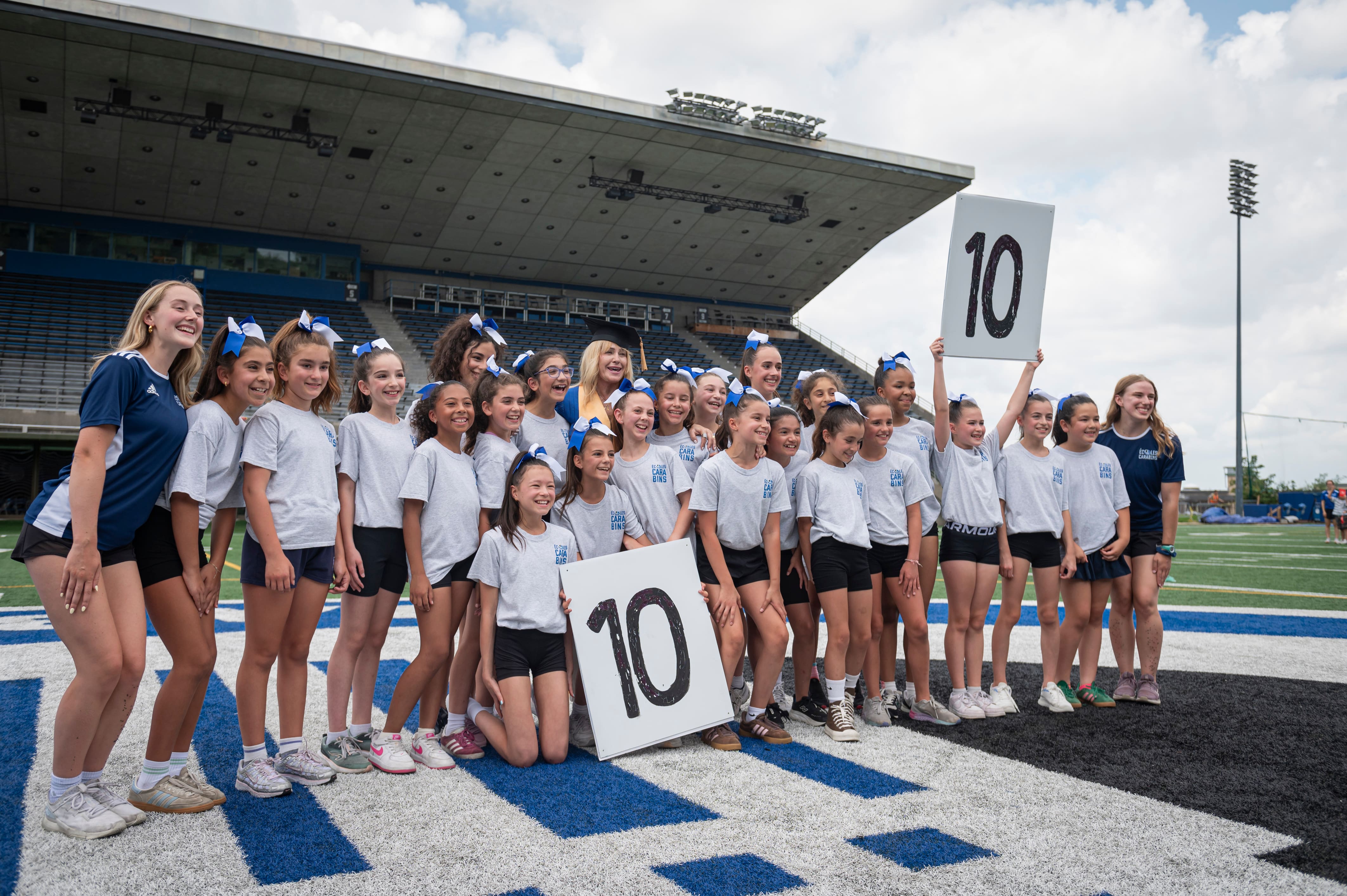 Nadia Comaneci (au centre) pose en compagnie d’une jeune équipe de cheerleading durant son passage à l’Université de Montréal, le vendredi 31 juillet 2026, afin d’y recevoir un doctorat honoris causa.