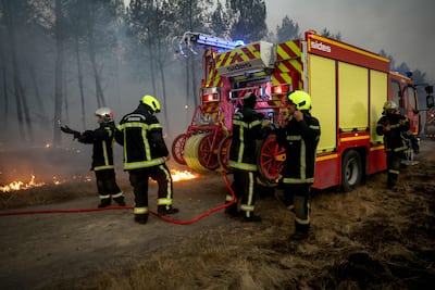 Firefighters stand near their vehicles as they battle a forest fire in Saint-Jean-d'Illac, about 30 km from Bordeaux, on July 26, 2026, while a forest fire ravages the forest north of the Arcachon Basin (Gironde).