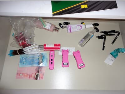 Foto de tres armas con pulso eléctrico rosa, jeringas y paquetes de plata que se encuentran en Daniel Alexander Franco-Murillo.