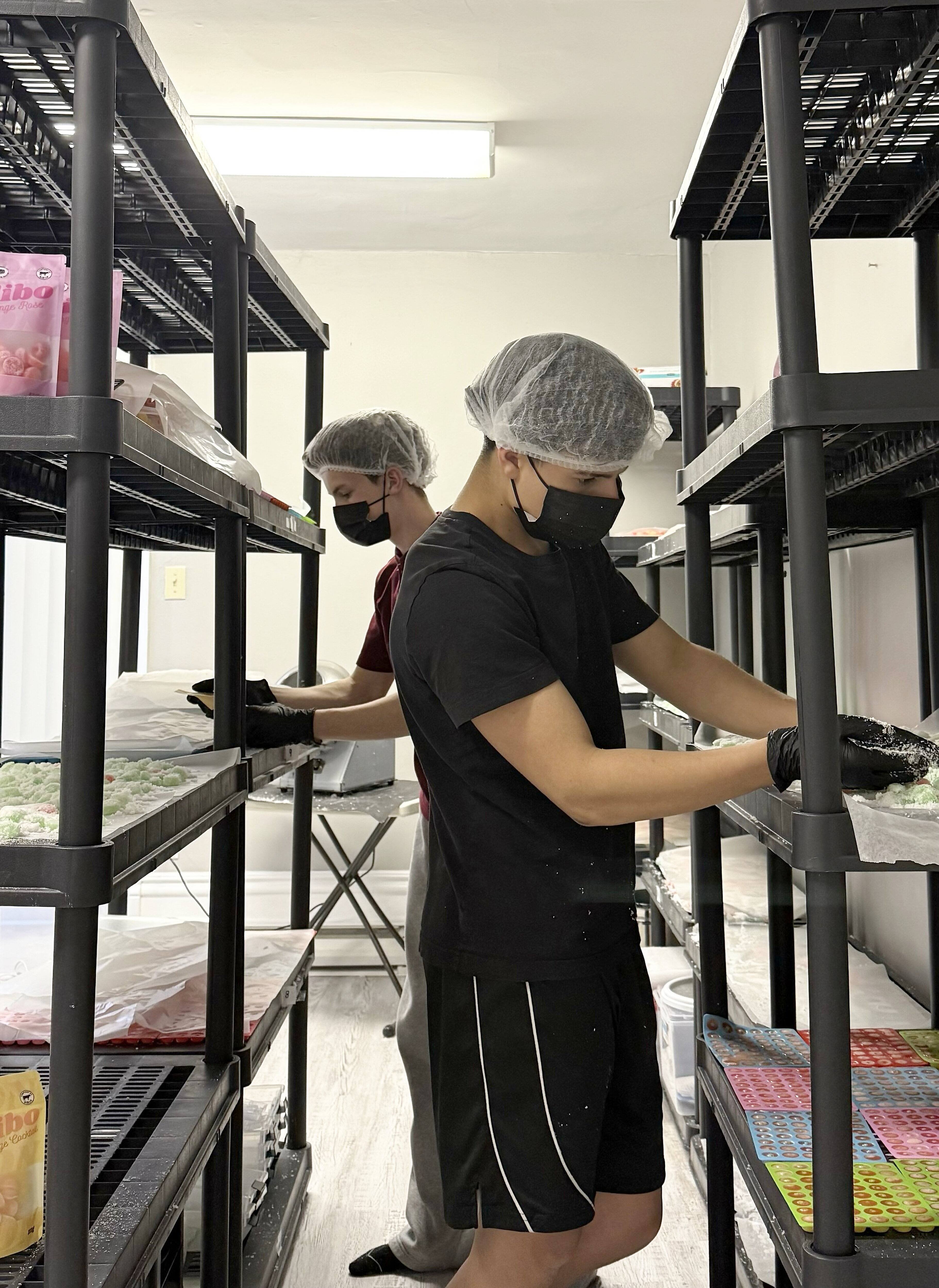 Emaël Smith et un de ses employés s’affairent à mouler des jujubes et à les enrober de sucre pendant une soirée de travail à l'atelier. Tous ses employés sont des collègues de classe qui ont aussi 16 ans et qui travaillent à temps partiel en même temps que leurs études.
