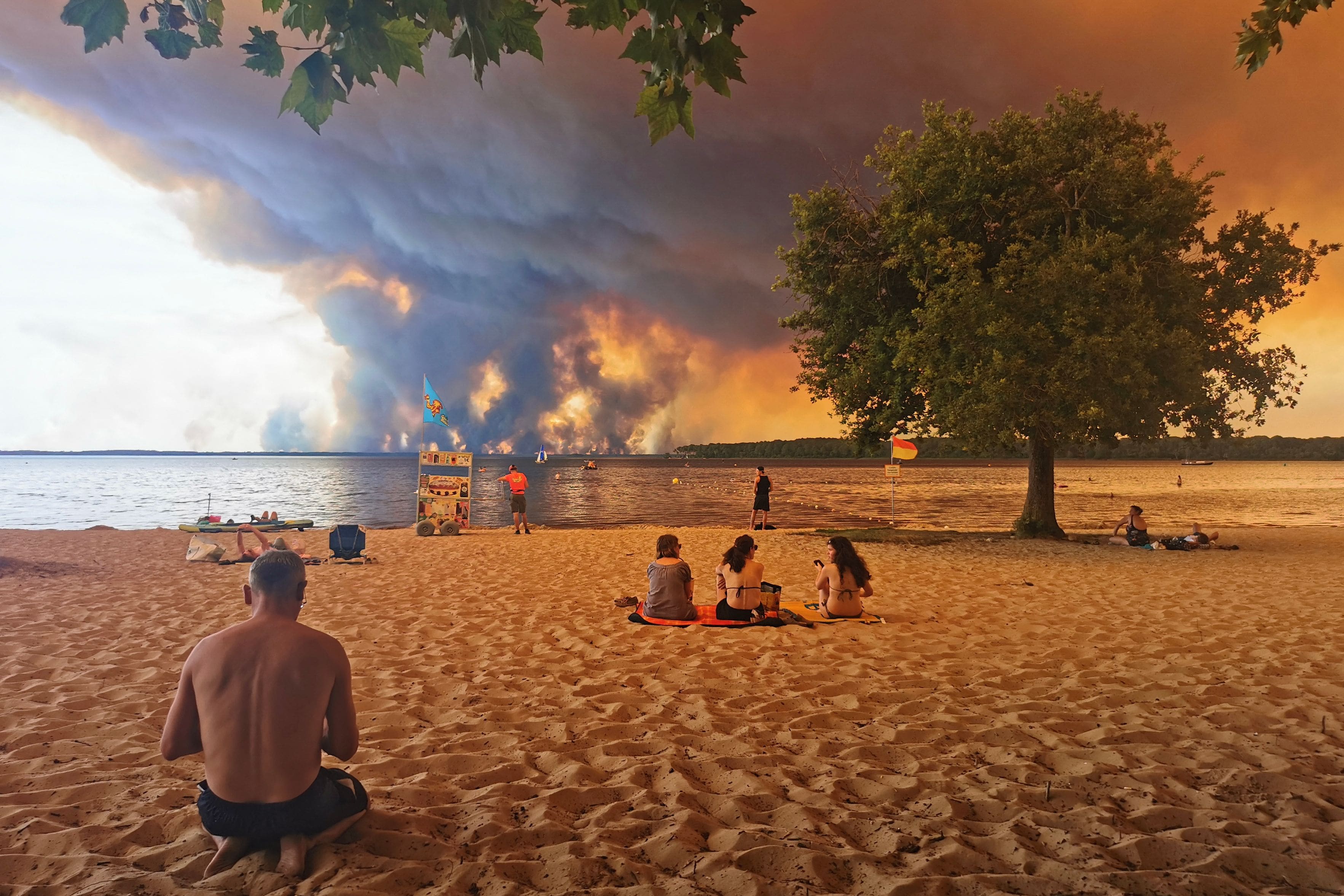 Holidaymakers sit on Moutchic beach in Lacanau, southwest France, July 24, 2026, as clouds of smoke rise into the sky from a forest fire.