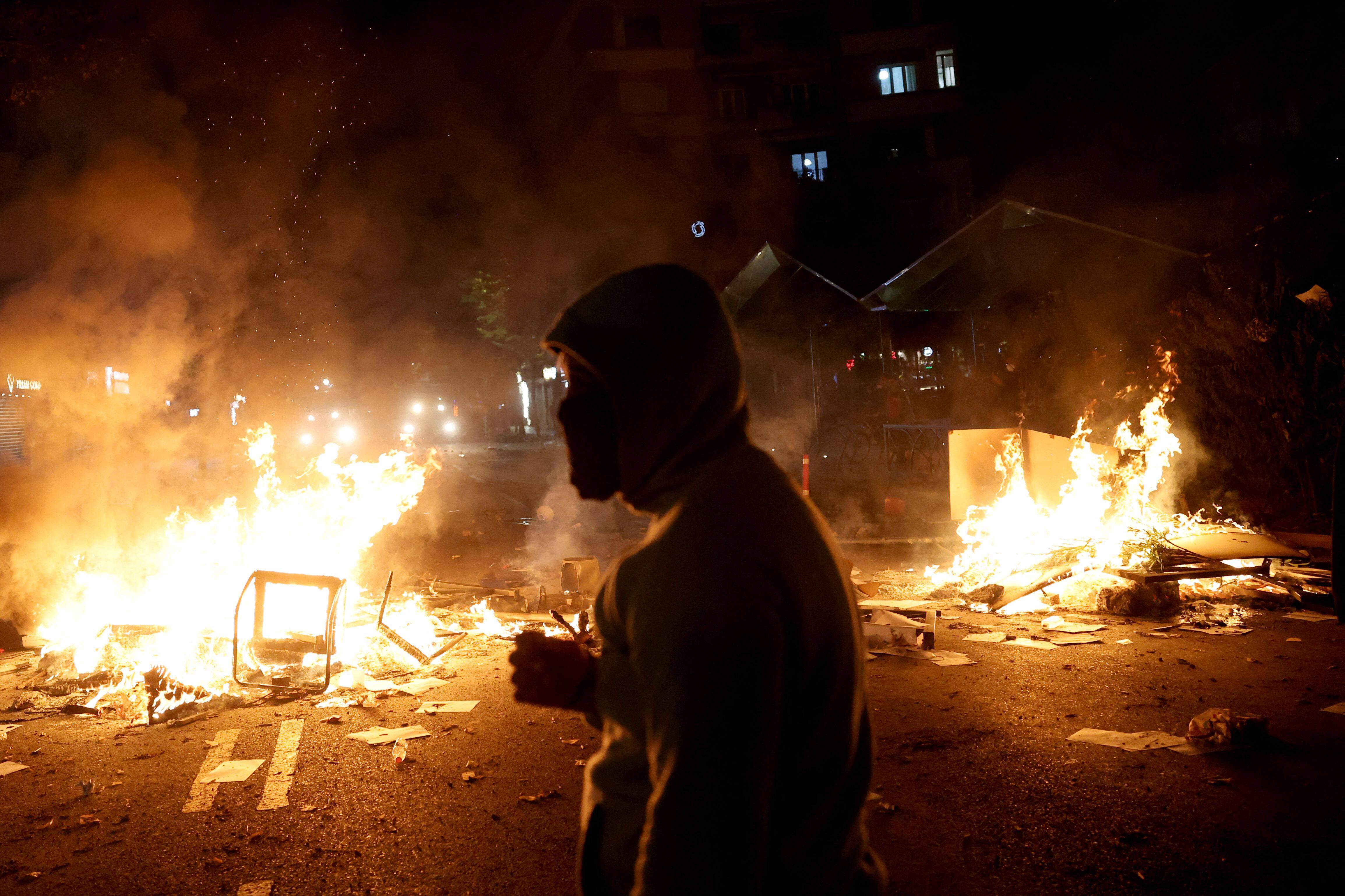 Un manifestant se tient près d'un incendie lors d'affrontements avec la police antiémeute sur la place Skanderbeg, pendant une manifestation à Tirana, en Albanie, le 13 octobre 2026.
