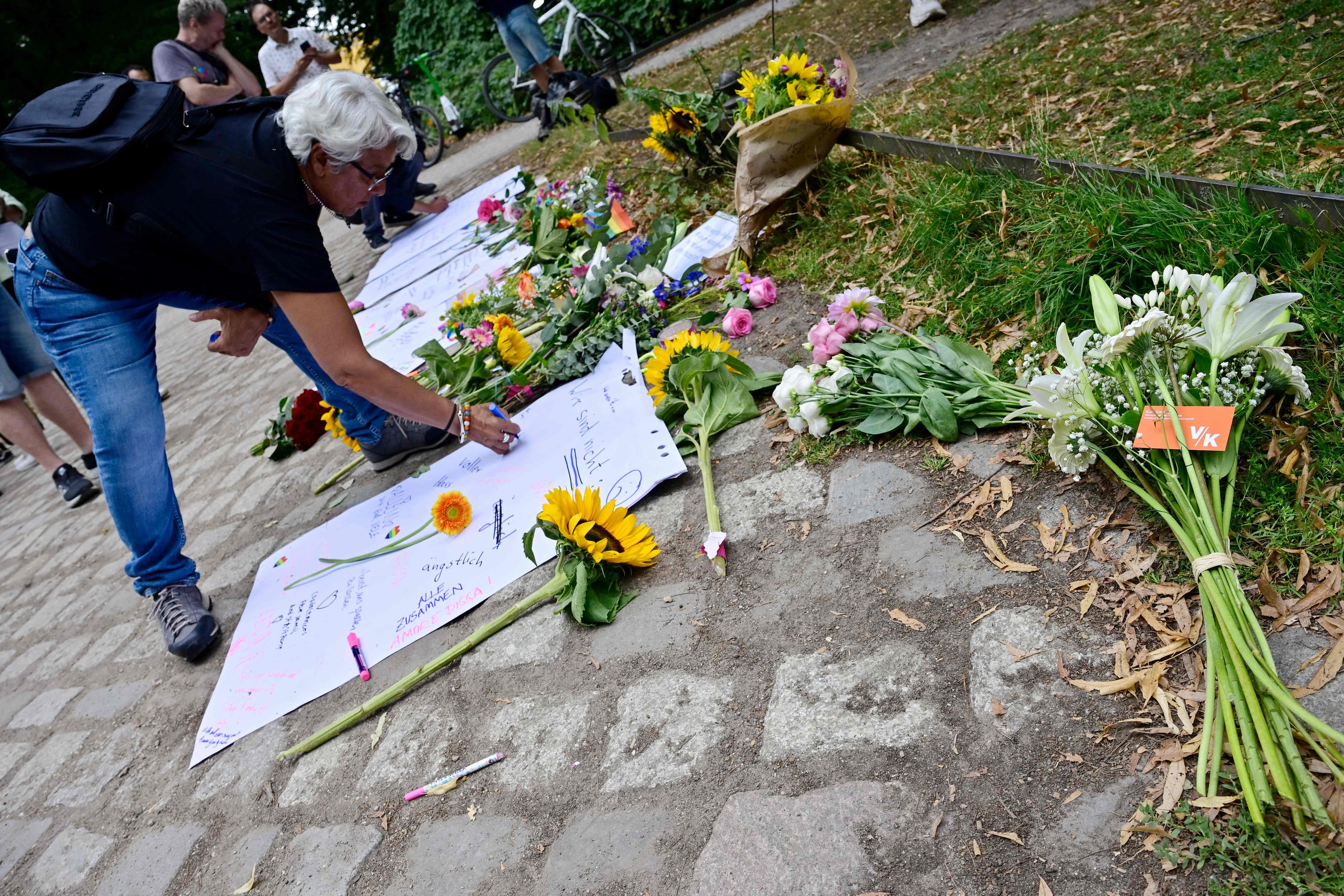 A passerby writes his thoughts on a paper placed on a makeshift memorial for the victims, July 26, 2026, near the site of Tiergarten park in Berlin, where a car had been thrown into people the day before, killing one person and injuring 16 others on the sidelines of the Christopher Street Day (CSD) parade.