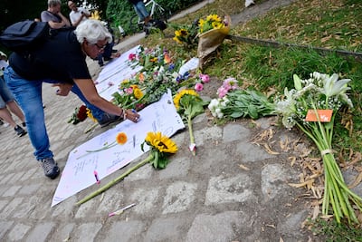 A passerby writes his thoughts on a paper placed on a makeshift memorial for the victims, July 26, 2026, near the site of Tiergarten park in Berlin, where a car had been thrown into people the day before, killing one person and injuring 16 others on the sidelines of the Christopher Street Day (CSD) parade.
