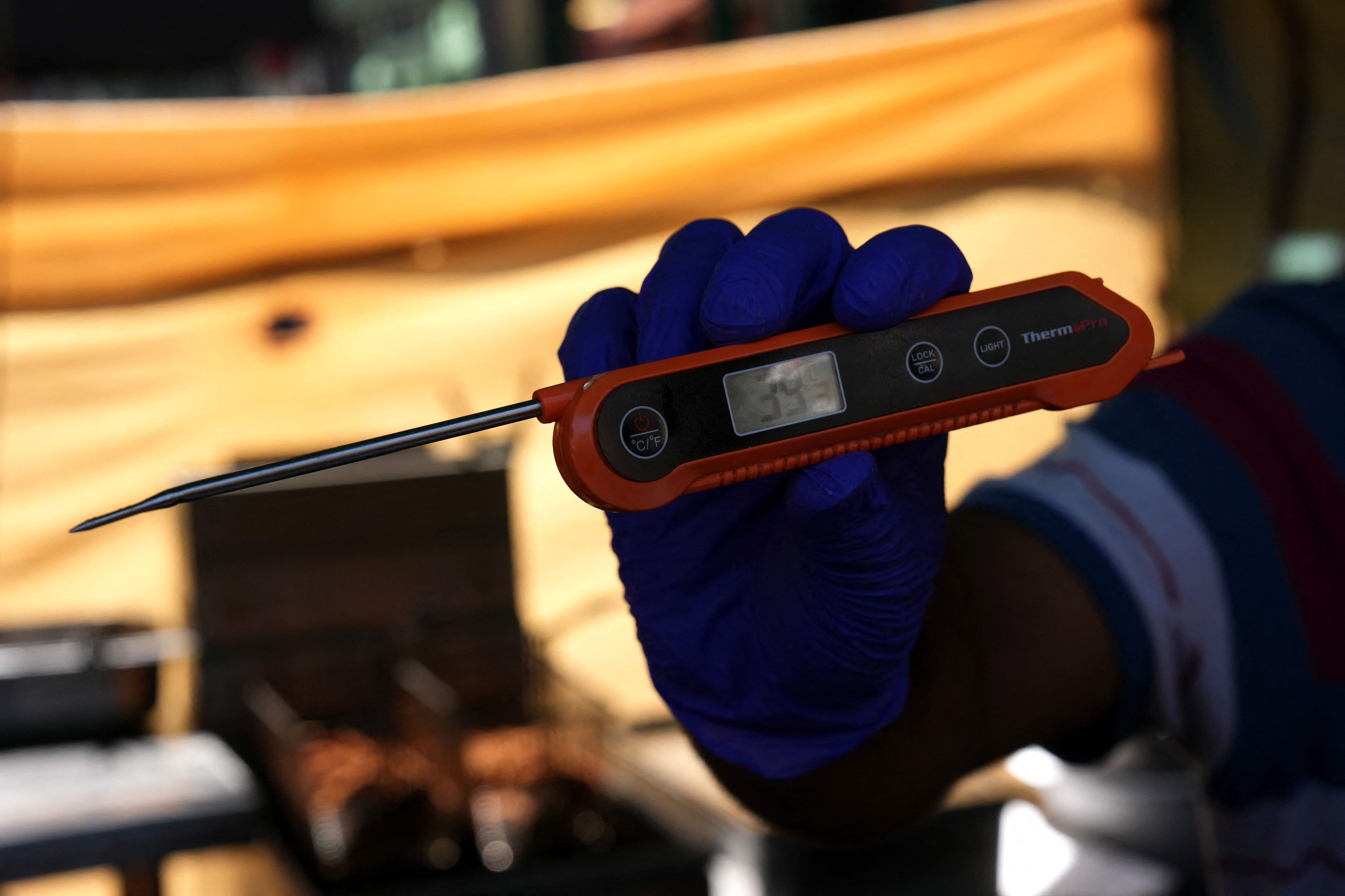 Un commerçant indique la température ambiante de 39 degrés Celsius, relevée à l'aide d'un thermomètre à viande ou alimentaire, à l'ombre de son étal au marché de Whitecross Street, dans l'est de Londres, le 26 juin 2026, en pleine vague de chaleur.