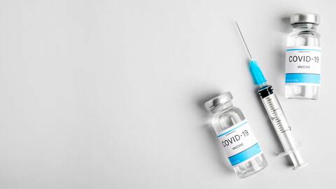 A female hand holds a bottle of Covid-19 vaccine on a blue background