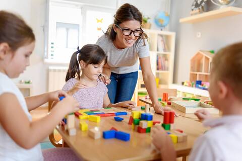 Preschool teacher with children playing with colorful wooden didactic toys at kindergarten