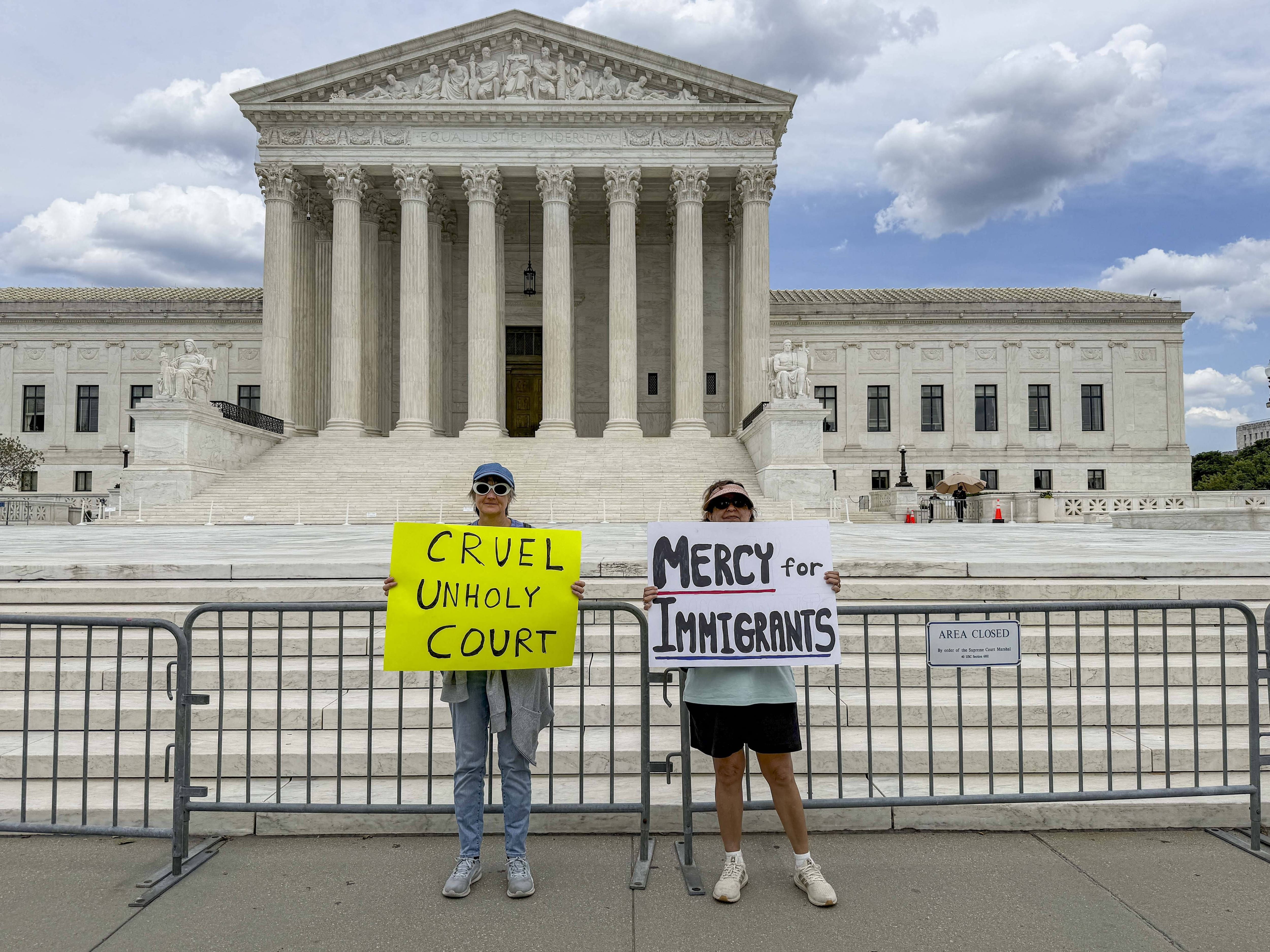 Two friends hold signs in front of the United States Supreme Court to denounce the ruling in Mullin v. Doe, which ends the temporary protection status enjoyed by approximately 350,000 Haitians and 6,000 Syrians.