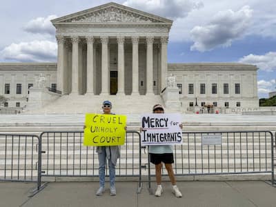 Two friends hold signs in front of the United States Supreme Court to denounce the ruling in Mullin v. Doe, which ends the temporary protection status enjoyed by approximately 350,000 Haitians and 6,000 Syrians.