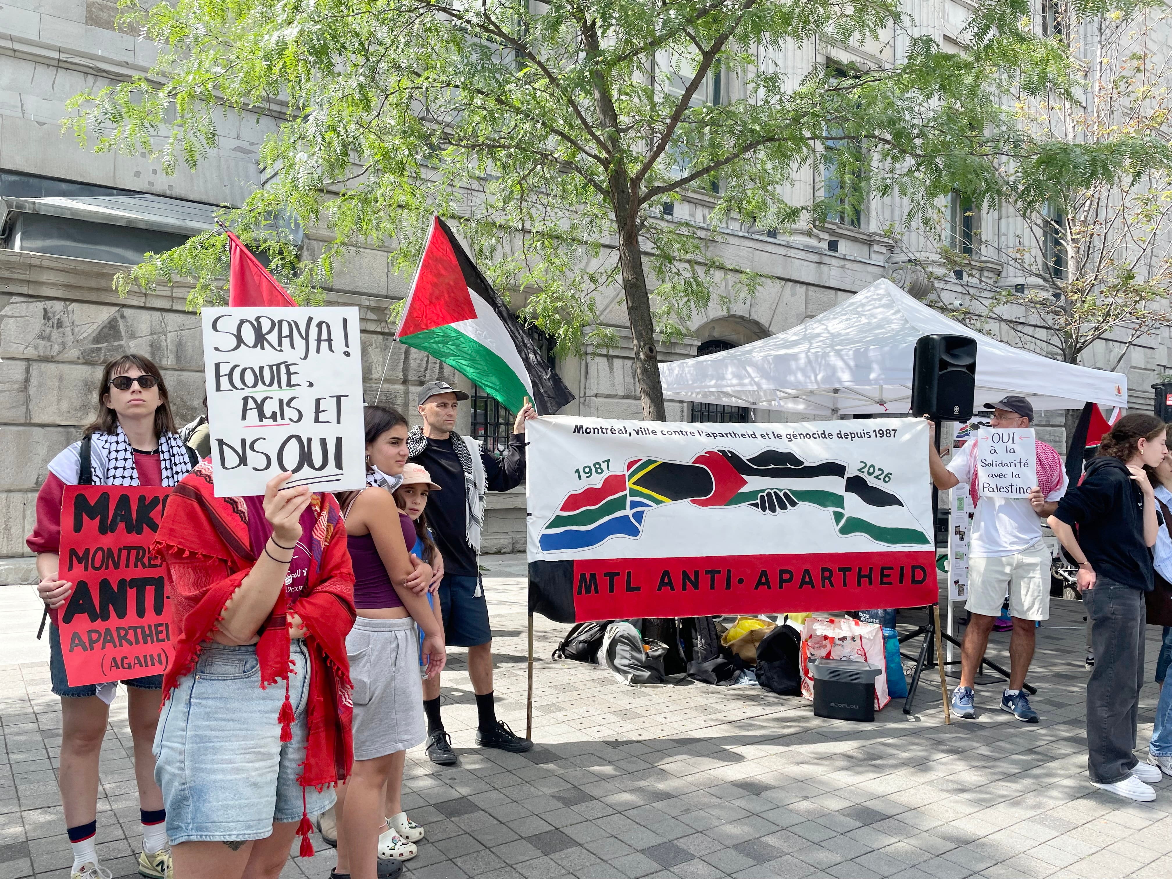 Des manifestants près d'une affiche Montréal Anti-Apartheid devant l'hôtel de ville de Montréal le lundi 24 août 2026. Au moins 70 personnes ont manifesté en appui à la motion de Projet Montréal en solidarité avec la Palestine.