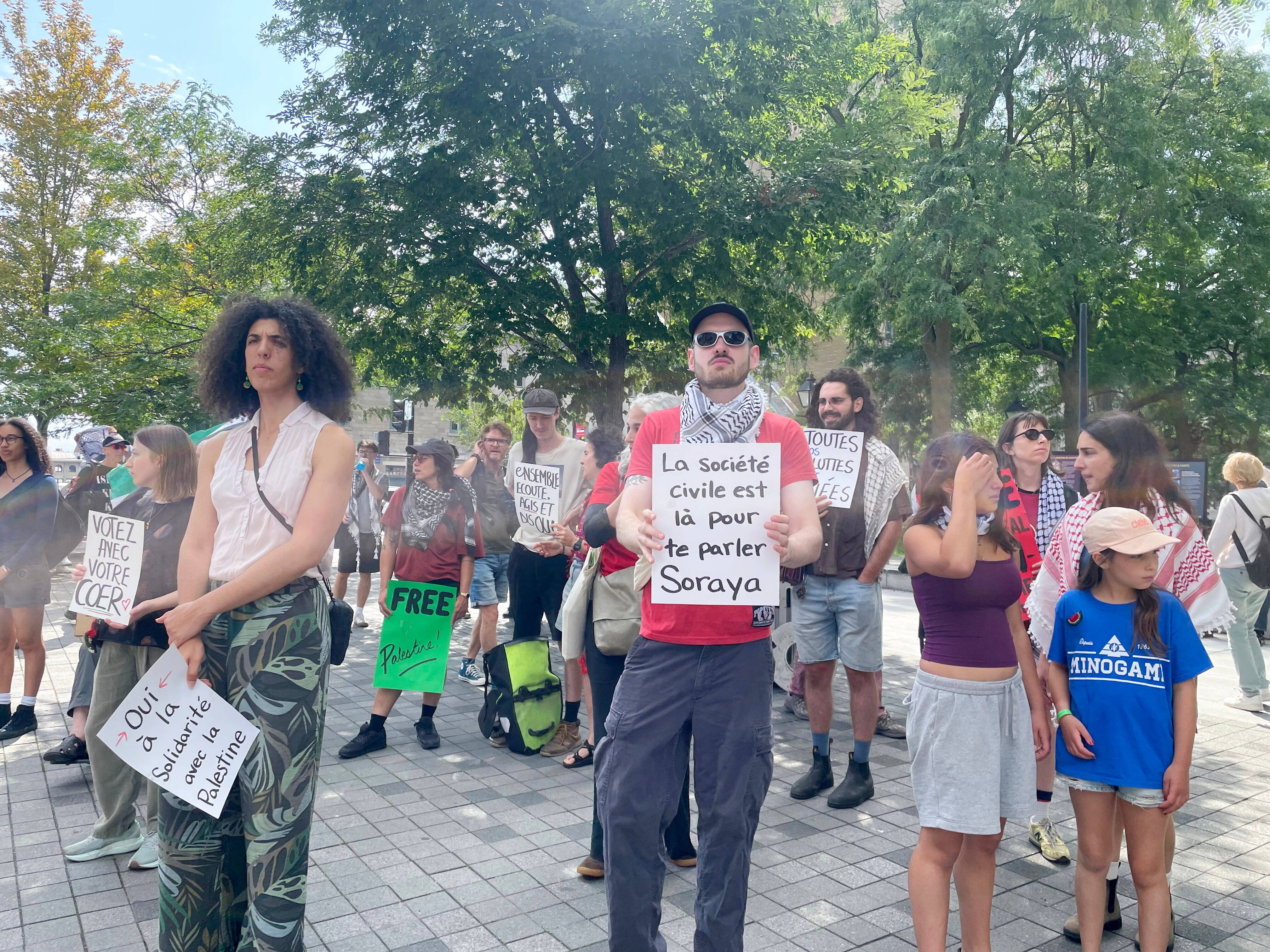 Des manifestants près d'une affiche Montréal Anti-Apartheid devant l'hôtel de ville de Montréal le lundi 24 août 2026. Au moins 70 personnes ont manifesté en appui à la motion de Projet Montréal en solidarité avec la Palestine.