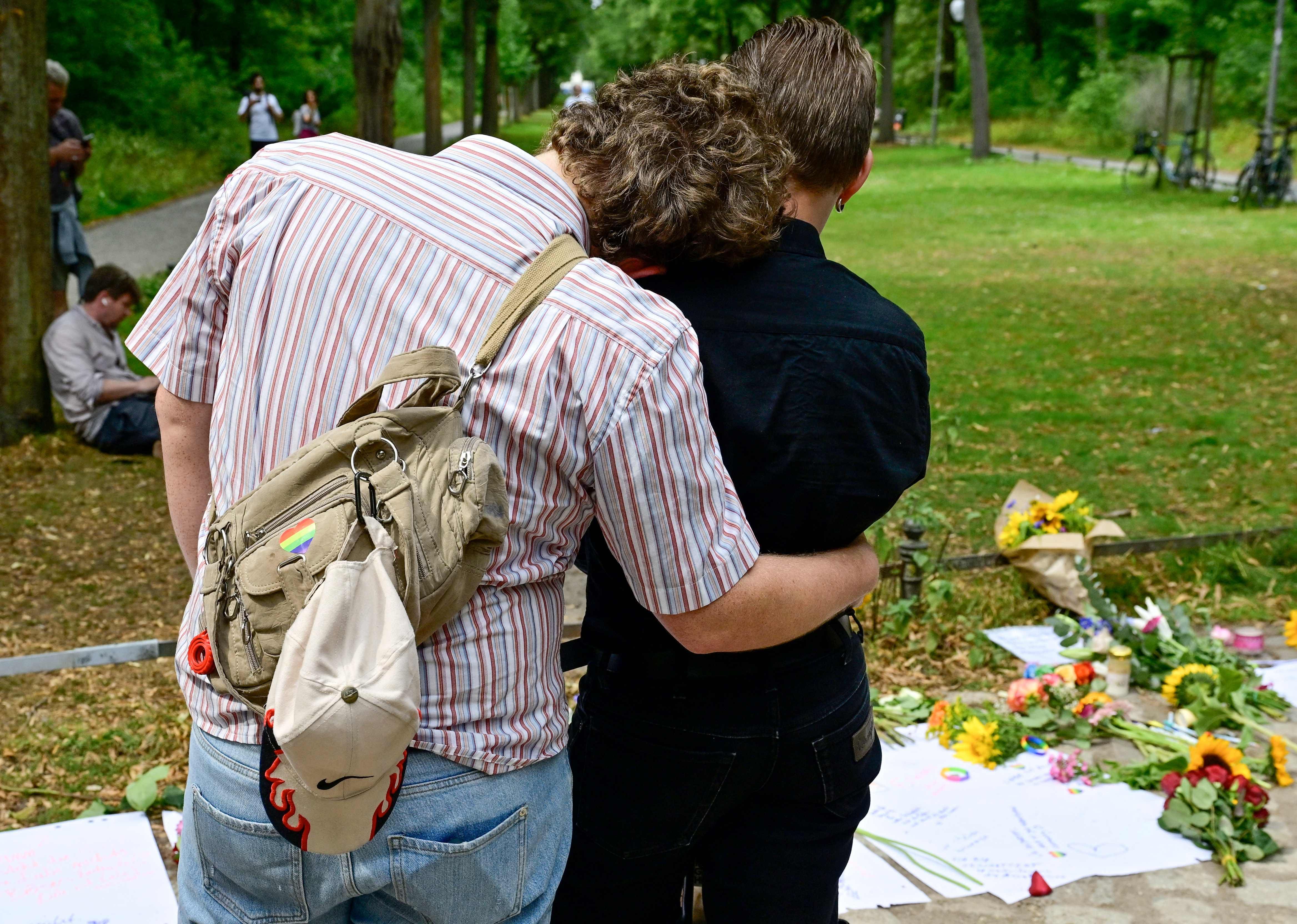 A couple embrace at a makeshift memorial site for the victims on July 26, 2026, near the scene in Berlin's Tiergarten park where a car was driven into people the previous evening, killing one person and injuring 16 others on the sidelines of the Christopher Street Day (CSD) parade.