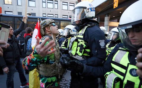 An opponent wearing a military helmet and jacket confronts a policeman who is blocking the fight.
