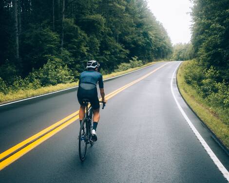Selective focus shot of professional road cyclist riding down wet and windy mountain road in forest, on aero road bike from carbon Selective focus shot of professional road cyclist riding down wet and windy mountain road in forest, on aero road bike from carbon