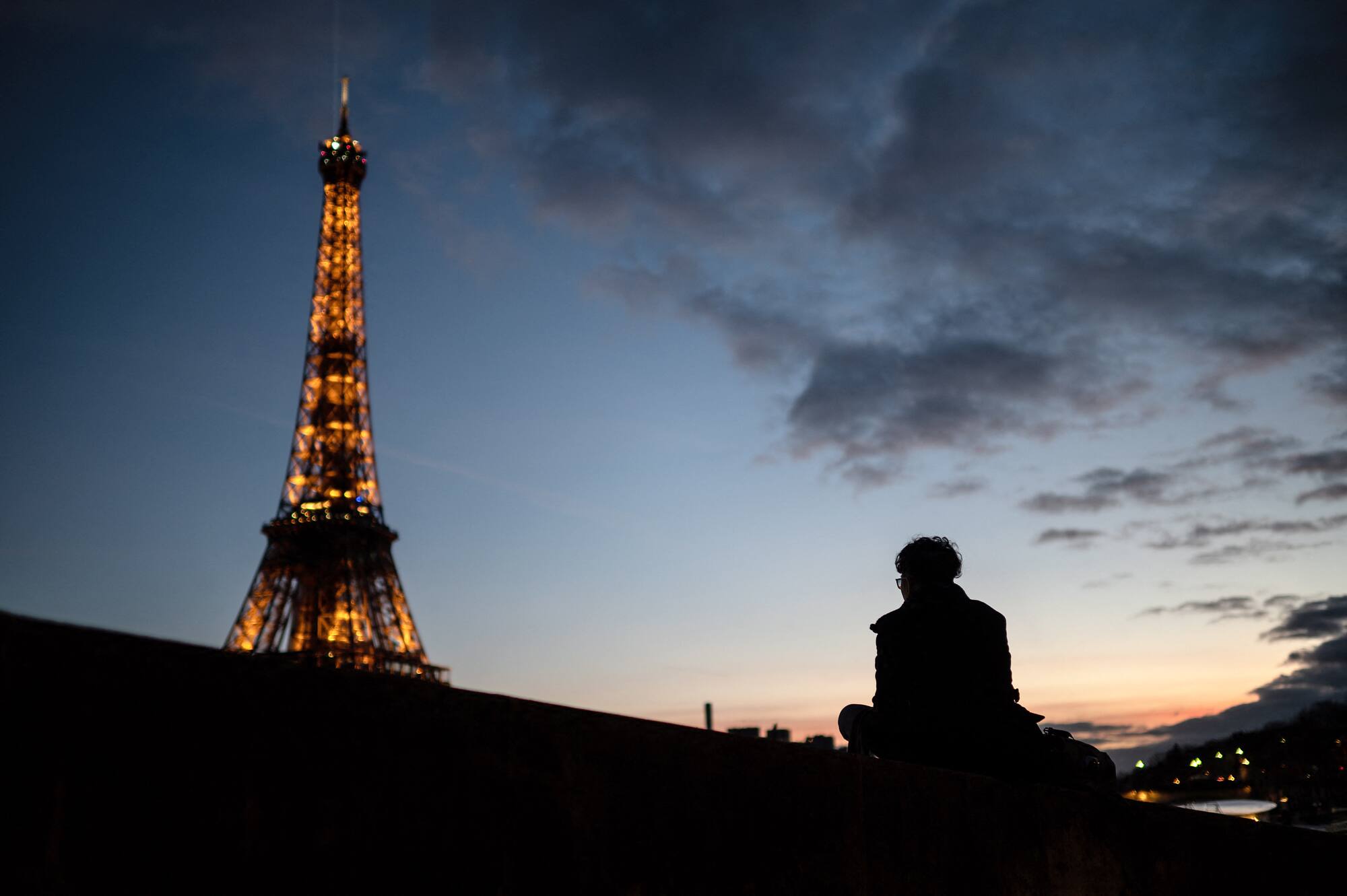 Sur cette photo, une adulte admire le coucher de soleil près de la tour Eiffel, à Paris.