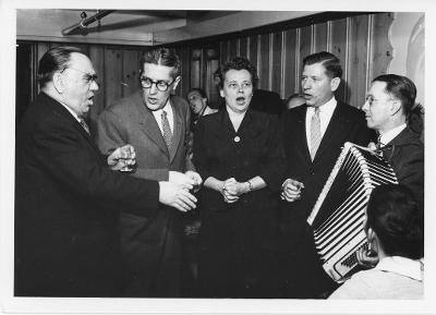 Les scientifiques chantent après le repas. De gauche à droite; Aleksandr V. Topchiev, Morton Grodzins, une femme inconnue (possiblement la femme de Howard F. Skidmore), Howard F. Skidmore et William A. Higinbotham à l’accordéon. PG 311 Cyrus S. Eaton Photographs, Western Reserve Historical Society, Cleveland, Ohio.