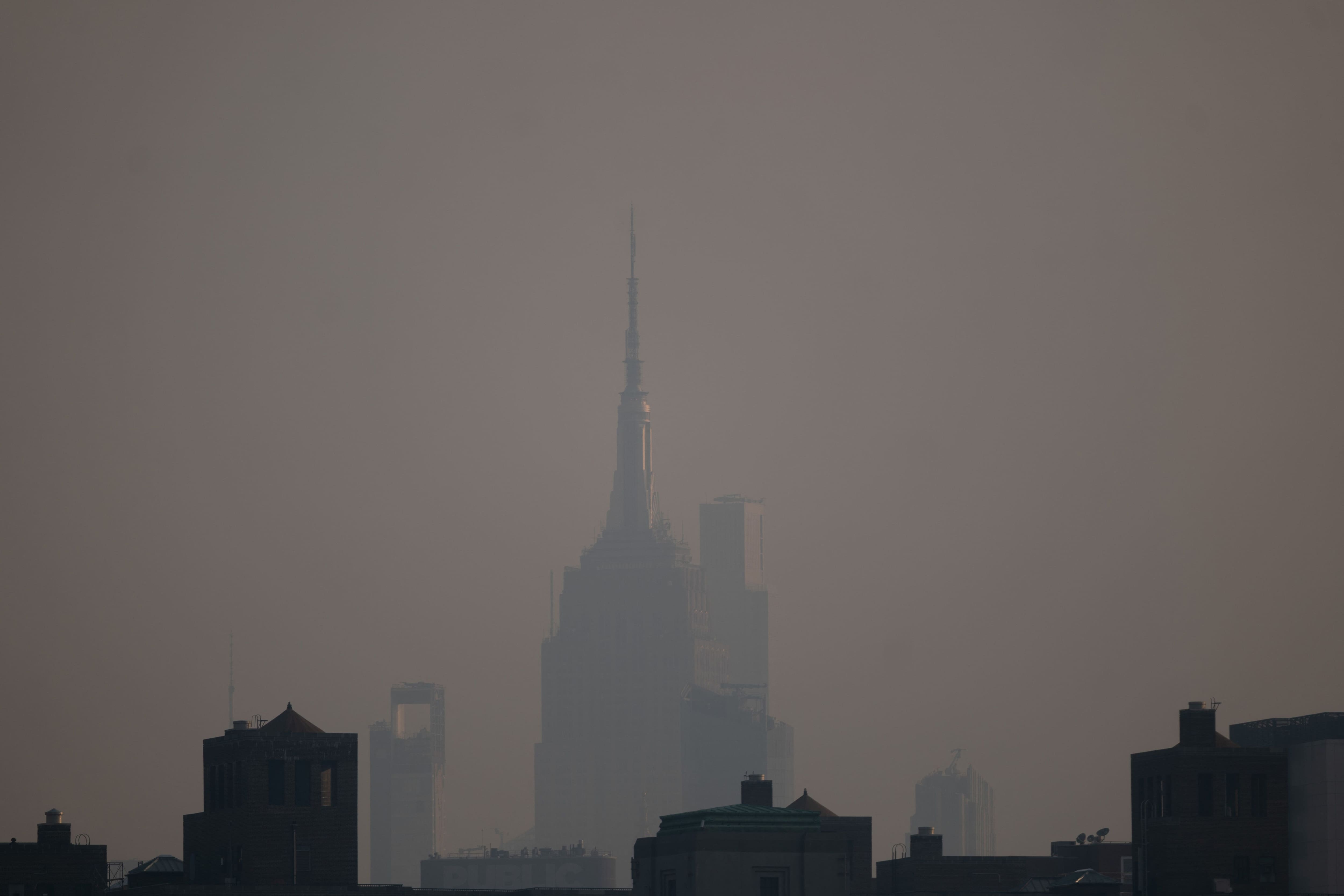 Haze from Canadian wildfires covers the Manhattan skyline, including the Empire State Building, as seen from Brooklyn Bridge Park on July 17, 2026 in New York. New York City is under an air quality health advisory as smoke from wildfires in Canada and the Great Lakes region gradually spreads across the region, creating a thick haze in the heat.