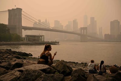 People sit near the Brooklyn Bridge as wildfire smoke from Canada causes a haze of smoke, July 16, 2026 in New York. Out-of-control wildfires raged Thursday in the Canadian province of Ontario, prompting evacuations and sending clouds of dangerous smoke toward the United States, where millions of people were exposed to unhealthy air.